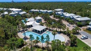 Eine Vogelperspektive zeigt ein Resort mit mehreren Gebäuden, einem zentralen Poolbereich und umliegenden Palmen.