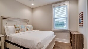 A bedroom with a bed, a nightstand, a window with blinds, and a wooden shelf.