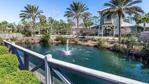 A waterfront property with a bridge, palm trees, and a building with a balcony. - 6 Seater Golf Cart, 5 Bikes! Zero Entry Pool & Beach! - Cool Your Jets at NatureWalk on 30A (Santa Rosa Beach)