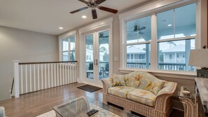 A spacious living room with a large window, a ceiling fan, and a wicker sofa. - 6 Seater Golf Cart, 5 Bikes! Zero Entry Pool & Beach! - Cool Your Jets at NatureWalk on 30A (Santa Rosa Beach)