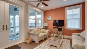A living room with a ceiling fan, a television, wicker furniture, and a view through a glass door. - 6 Seater Golf Cart, 5 Bikes! Zero Entry Pool & Beach! - Cool Your Jets at NatureWalk on 30A (Santa Rosa Beach)