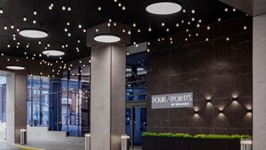 A modern hotel entrance with a dark facade, illuminated signage, and a series of hanging lights. - Four Points by Sheraton Flushing (Flushing)