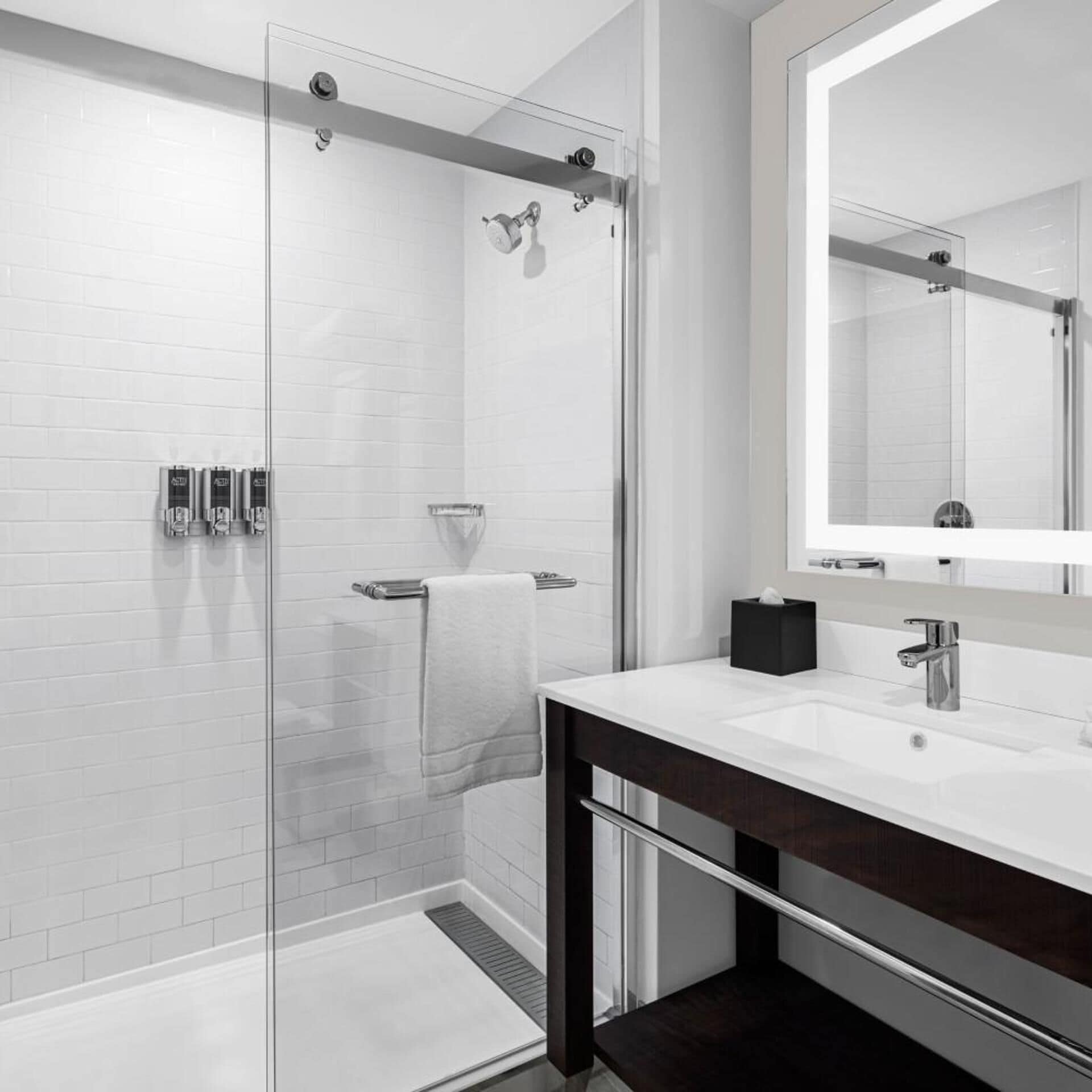 A modern bathroom with a glass-enclosed shower, a white sink with a dark vanity, and a large mirror.