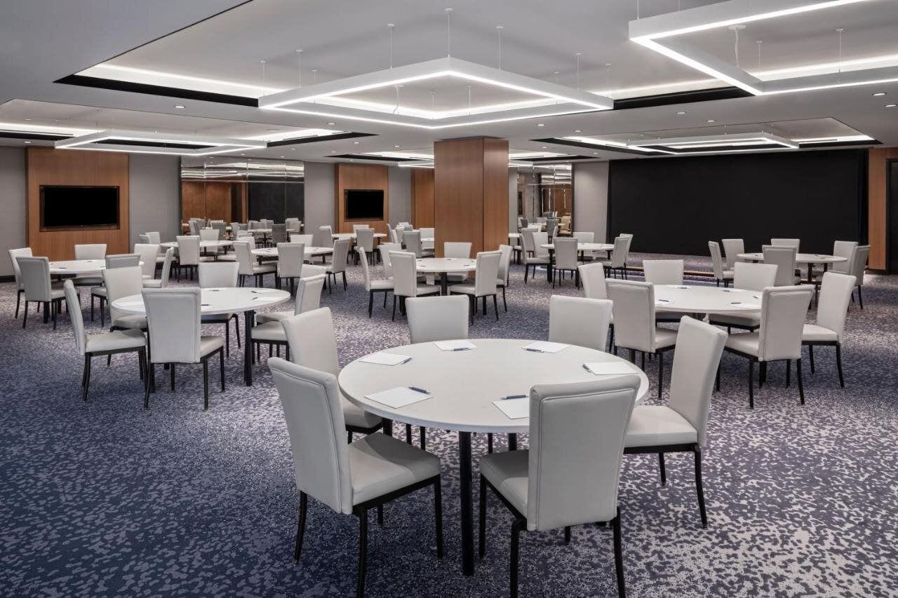 A conference room with multiple round tables and chairs, a large screen, and a carpeted floor.