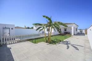 A courtyard with a white picket fence, a palm tree, and a building with a tiled roof.