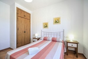 A bedroom with a bed, wooden wardrobe, two bedside tables with lamps, and two framed pictures on the wall.