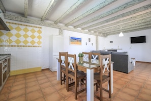 A kitchen with a dining table and chairs, a refrigerator, and a TV mounted on the wall.