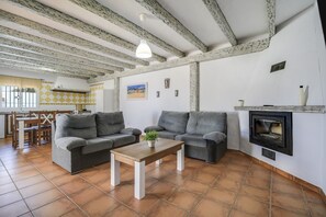 A living room with two grey sofas, a wooden coffee table, a fireplace, and a dining area with a table and chairs.