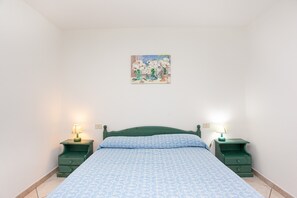 Ein Schlafzimmer mit einem Bett, zwei Nachttischen mit Lampen, einem Wandbild und einem Fliesenboden.
