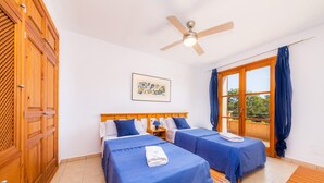 A room with two beds, a ceiling fan, a window with curtains, and a wooden wardrobe.
