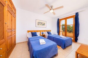 Ein Zimmer mit zwei Betten, einem Deckenventilator, einem Fenster mit Vorhängen und einem Holzschrank.