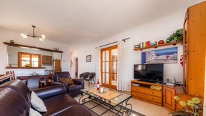 A living room with a leather sofa, a glass coffee table, a TV, and a kitchen area with a dining table and chairs.