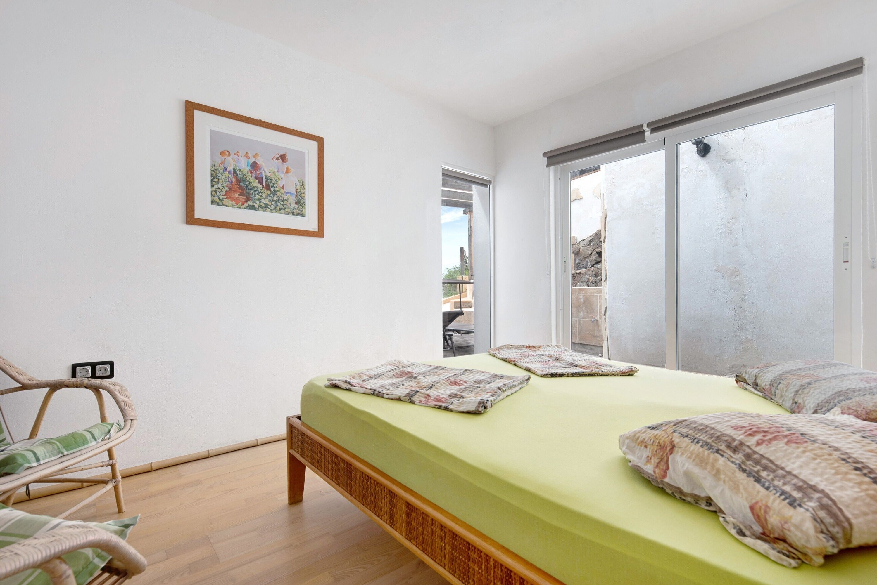 A bedroom with a bed, a chair, a framed picture, and a sliding door.
