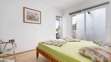 A bedroom with a bed, a chair, a framed picture, and a sliding door.