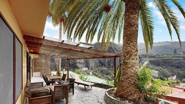A covered outdoor seating area with stone flooring, wooden furniture, and a view of a mountainous landscape. - Apartament Ana with Mountain View, Sea View, Wi-Fi & Terrace (San Marcos)