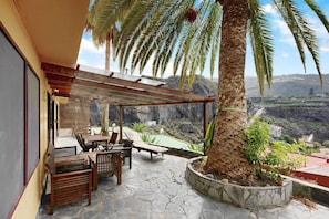 Un espace extérieur aménagé, abrité et doté d’un sol en pierre, de mobilier en bois et offrant une vue sur un paysage montagneux.