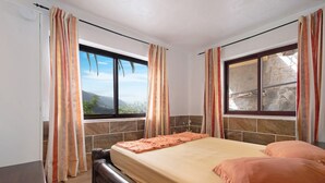 A bedroom with a bed, curtains, a window with a stone wall, and a view of the outdoors. - Apartament Ana with Mountain View, Sea View, Wi-Fi & Terrace (San Marcos)