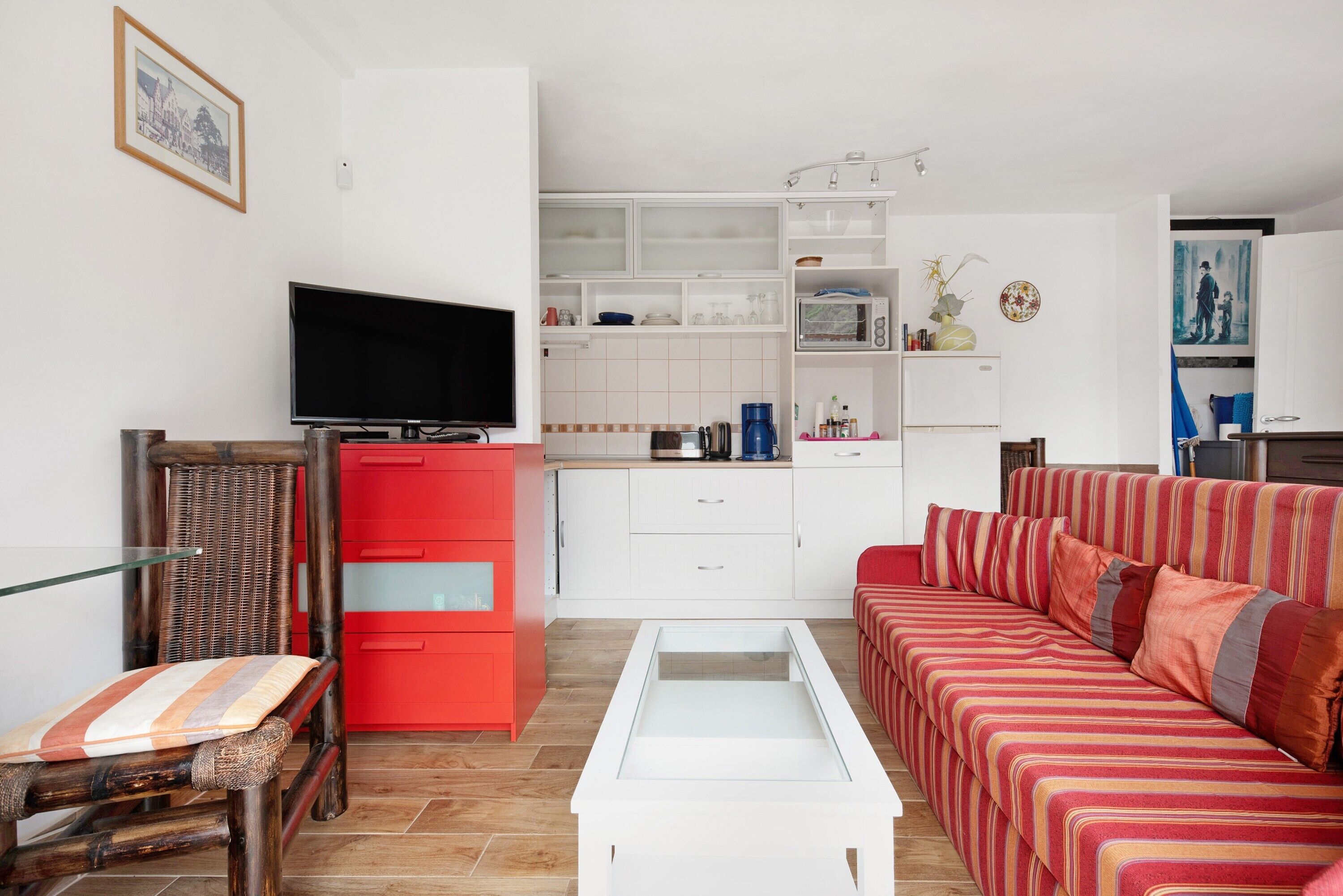 Un salon moderne avec un téléviseur à écran plat, un meuble rouge, un canapé à rayures et une table basse en verre.