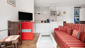 Una sala de estar moderna con un televisor de pantalla plana, un mueble rojo, un sofá a rayas y una mesa de centro de vidrio.