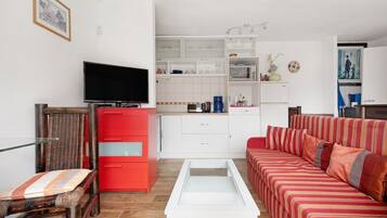 Un salon moderne avec un téléviseur à écran plat, un meuble rouge, un canapé à rayures et une table basse en verre.