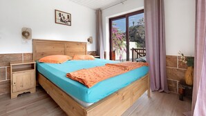 Un dormitorio con cama de madera, mesita de noche, ventana con cortinas, lámpara de pared y una pequeña mesa con un florero.
