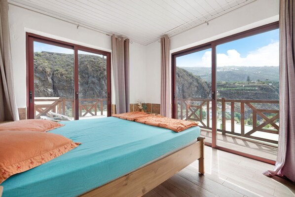 A bedroom with a bed, curtains, and a balcony with a view of a mountainous landscape.