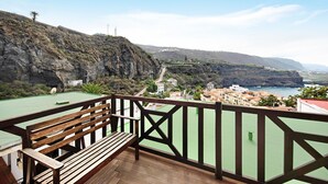 Un banco de madera en un balcón con vistas a un pueblo costero, edificios y acantilados.