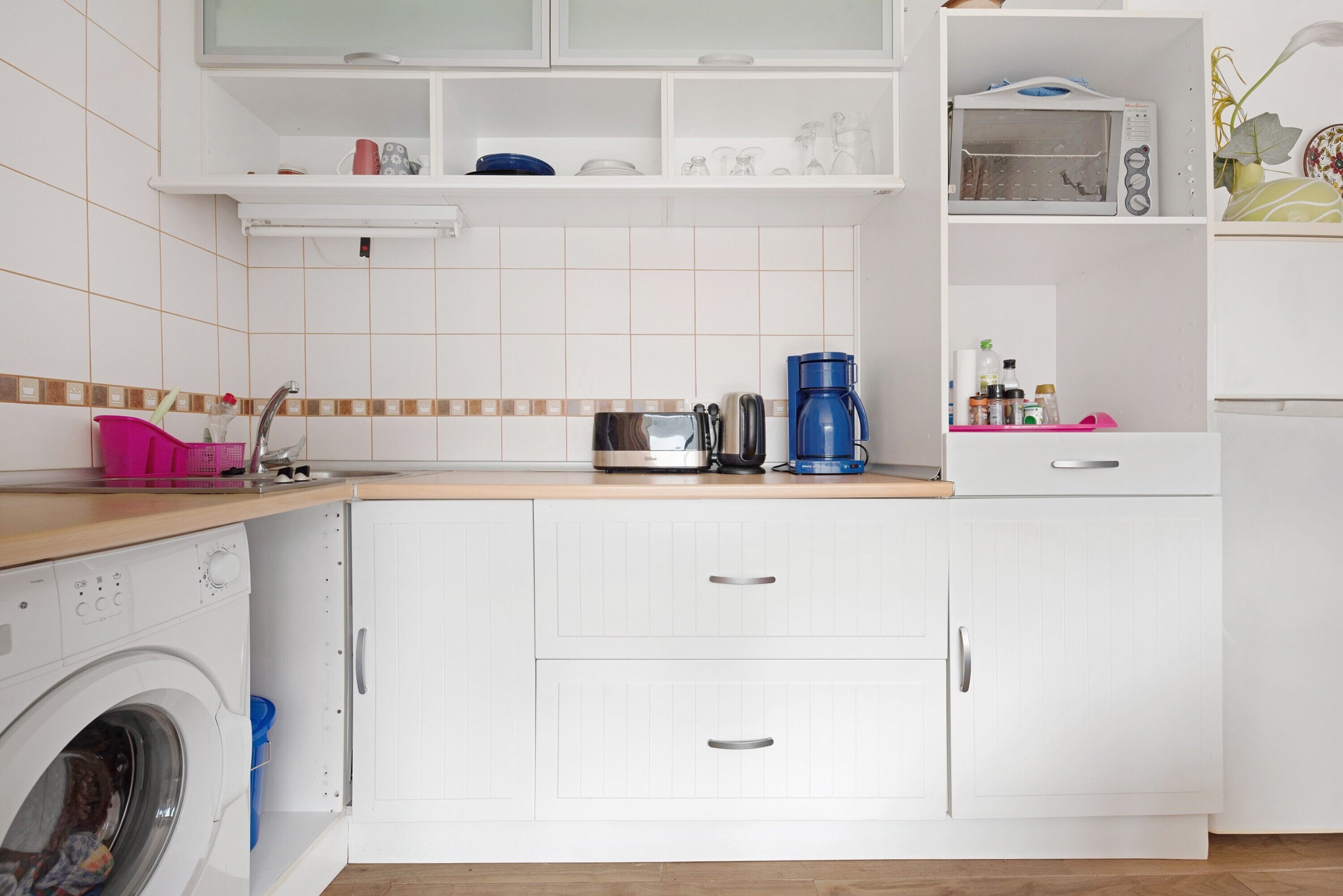 Une cuisine moderne équipée d’un lave-linge, de meubles blancs et d’une machine à café.