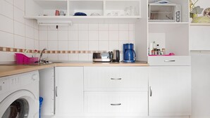 Una cocina moderna con lavadora, armarios blancos y cafetera.