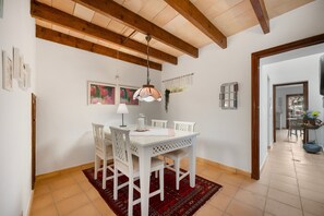 A dining area with a white table, chairs, and a red patterned rug. There is a ceiling fan and a wall-mounted light fixture. - Holiday Home Casa Maria Angela with Sun Terrace, Patio and Wi-Fi (Arta)