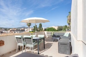 Een terras met buitenmeubilair, een tafel, stoelen en een parasol.