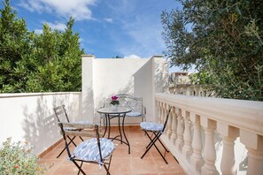 Eine Terrasse mit Tisch und zwei Stühlen, umgeben von Grünpflanzen und einer weißen Mauer.