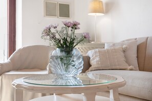 Un salon avec une table en verre sur laquelle est posé un vase de fleurs, un canapé et une lampe.