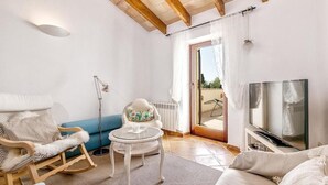 Une pièce chaleureuse avec un fauteuil à bascule, une petite table ronde, un canapé, un téléviseur et une porte-fenêtre coulissante donnant sur un espace extérieur.