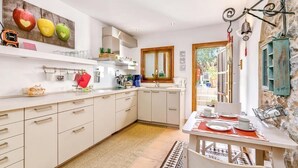 Une cuisine moderne avec des meubles blancs, un coin repas avec une table dressée pour quatre personnes et un mur en pierre au style rustique.