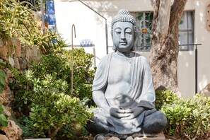 Eine sitzende Buddha-Statue, umgeben von Grünpflanzen und einem Baum.