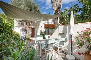 Un espace extérieur aménagé en patio, avec une table et des chaises, entouré de plantes et d’une statue.