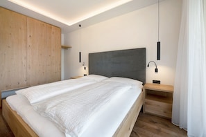 A modern bedroom with a large bed, wooden wardrobe, bedside tables, and pendant lighting.