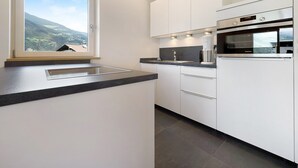 Una cocina moderna con horno integrado, ventana con vistas al campo y muebles de cocina blancos.