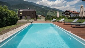Una piscina con sillas de descanso y sombrillas, rodeada de casas y montañas.