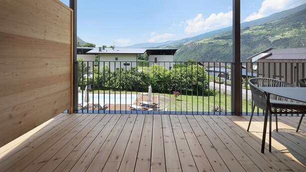 Una terraza de madera con vistas a una piscina, un patio y un paisaje montañoso.