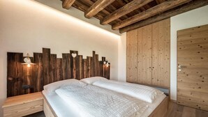 A bedroom with a wooden headboard, a bench, and a wardrobe. - Apartment 'Sommersbergerhof' with Mountain View, Shared Pool and Wi-Fi (Brixen)