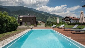 A swimming pool with a wooden deck, lounge chairs, and a mountainous backdrop. - Apartment 'Sommersbergerhof' with Mountain View, Shared Pool and Wi-Fi (Brixen)