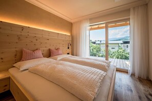 Un lit double avec une tête de lit en bois, une table de chevet et une vue sur un balcon doté d’une balustrade.