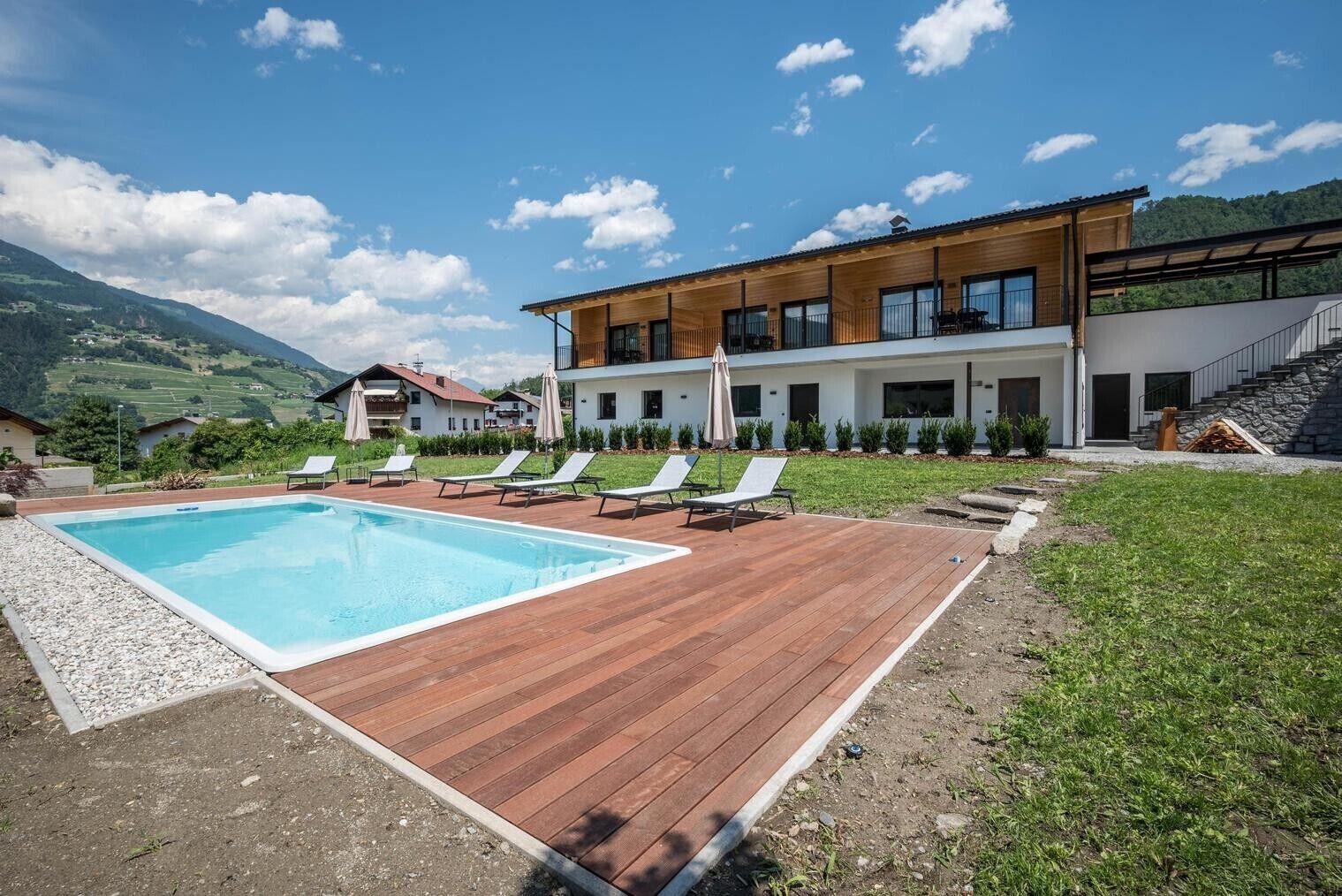 Un edificio moderno con piscina, sillas de descanso y montañas al fondo.