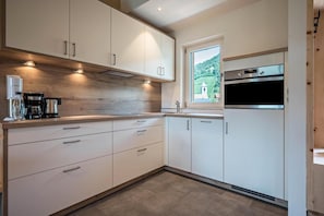 Une cuisine moderne avec des meubles blancs, un four encastré et une fenêtre donnant sur un paysage verdoyant.