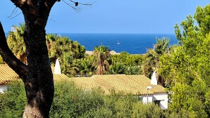 Vista costera amb cel serè, una embarcació a l'aigua i vegetació abundant.