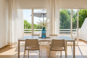 A dining area with a table, chairs, a vase with flowers, and a view of greenery outside. - Apartment 'Villa Orchidée - Coves Noves' with Sea View, Wi-Fi and Air Conditioning and terrace (COVES NOVES)