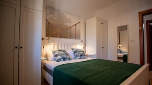 Ein Schlafzimmer mit einem Bett, Nachttischen, einer Hängeleuchte, einem Kleiderschrank und einem Spiegel.