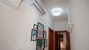 Ein Flur mit Klimaanlage, einer Deckenleuchte und gerahmten Kunstwerken an der Wand.
